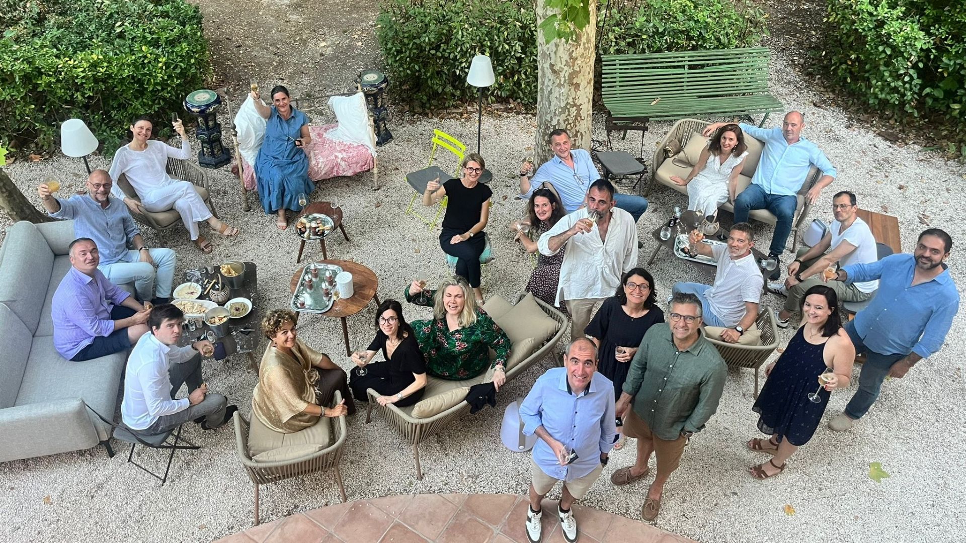 Vue aérienne des invités partageant un apéritif chic dans un jardin aménagé avec des salons extérieurs, lors d’un anniversaire sous tente en maison de famille.